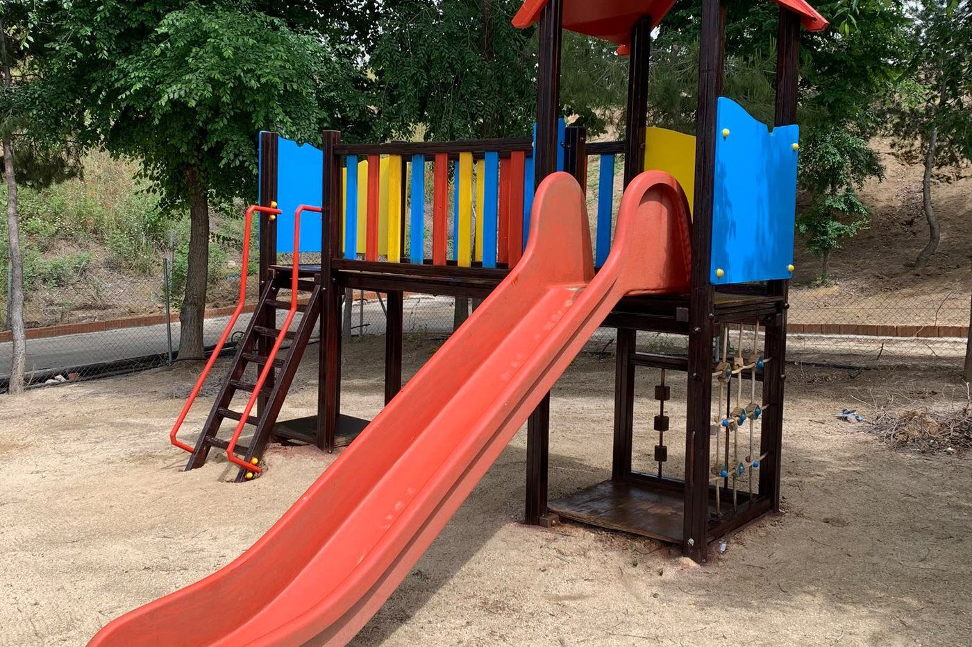 Torre de juegos con tobogán, a la sombra de los árboles